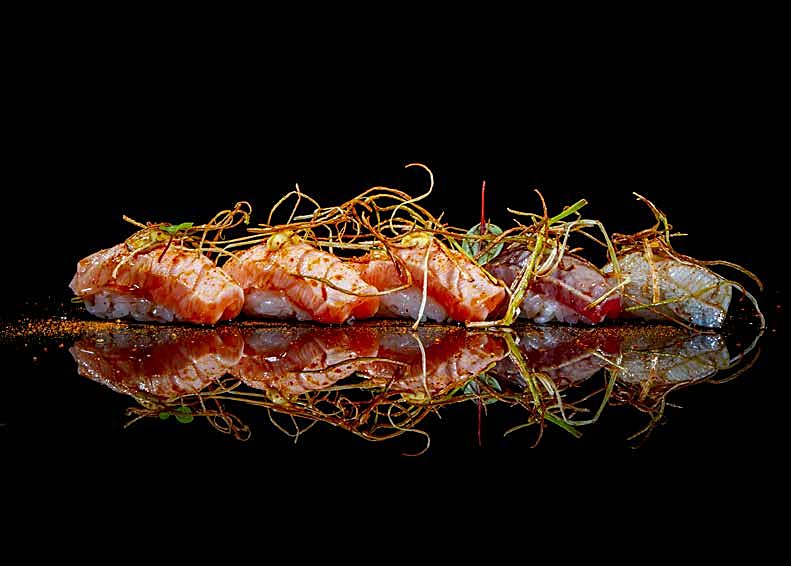 Nigiri scottati con fili di porro croccante, riflessi sul nero